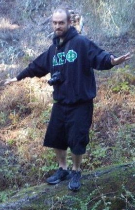 Paul standing on a log with his Delta Sigma Phi sweatshirt and DSLR camera